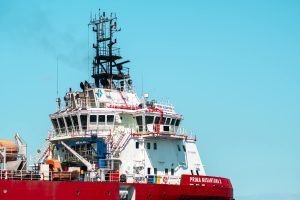 Red and white tugboat Prima Nusantara X in Makassar harbor, South Sulawesi, under a clear blue sky.