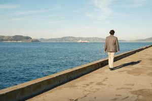 A man walks along a pier overlooking the ocean in Los Angeles, California during a sunny day.