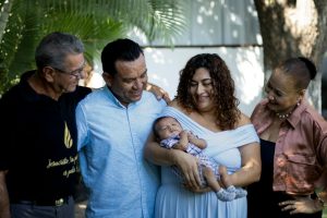 Joyful family gathering with proud parents and grandparents holding a newborn baby outdoors.