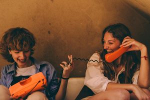 Two friends enjoy a light-hearted conversation using a retro orange phone in an intimate setting.