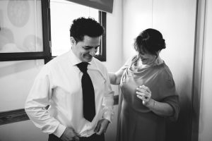 Heartwarming moment of a mother assisting her adult son in getting ready, captured in black and white.