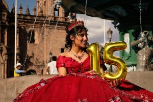 A young woman celebrates her 15th birthday in a vibrant red gown by a historic fountain.