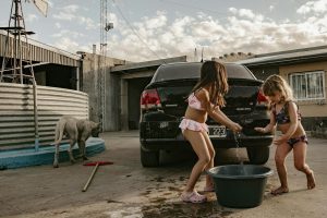 Two kids enjoy a water play in a sunny backyard with a dog nearby.
