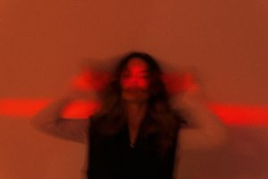 Blurred portrait of a person in red and orange lighting, creating a dreamlike effect.