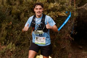 Young male trail runner enthusiastically giving a thumbs up during an outdoor race through forest.