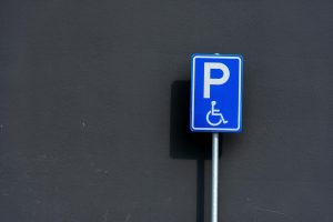 A blue disabled parking sign mounted on a metal pole against a dark wall.