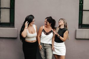 Three adult women smiling and interacting casually against an outdoor wall in Argentina.