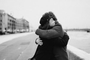Black and white scene of a couple hugging by the waterfront in winter, capturing love and happiness.