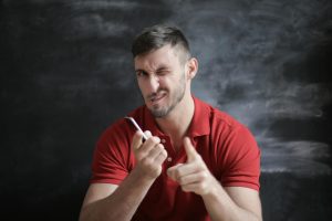 Confident man in red polo shirt winks and points in front of a chalkboard.