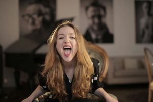 Portrait of a young woman with blonde hair expressing emotions while sitting indoors.