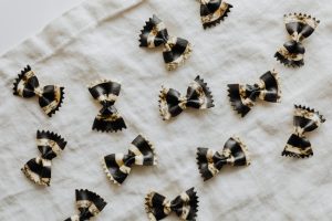Top view of black and white bow tie pasta on white cloth, showcasing unique patterns.
