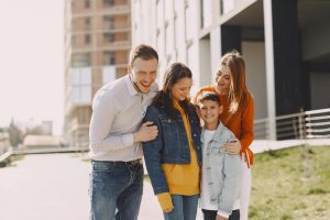 Delighted family in trendy casual wear holding each other and standing near modern building on city street while walking together during weekend
