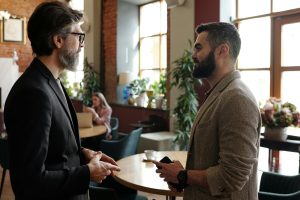 Two bearded men engage in a professional conversation in a stylish cafe interior.