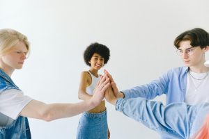 Group of cheerful multiethnic teenager friends in denim wear holding hands stacked standing on white background