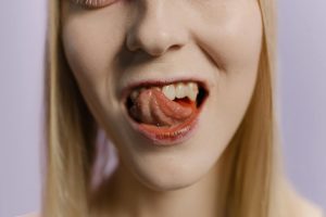 Close-up portrait of a blonde woman with her tongue out against a neutral background.