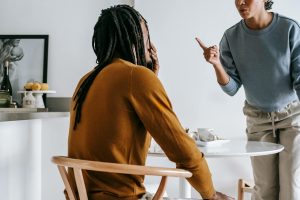 Young African American lady standing near table while having argument with guy sitting at kitchen