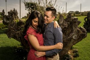 A loving couple embraces in a sunny outdoor setting surrounded by nature.