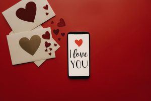 Smartphone with 'I Love You' display surrounded by red hearts and envelopes.
