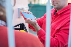 A delivery person in a red jacket uses a smartphone to confirm a package delivery.