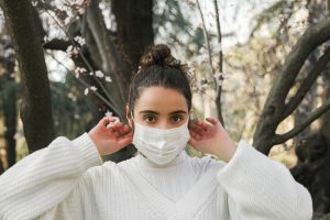 Portrait of a young woman wearing a face mask in a springtime forest setting.