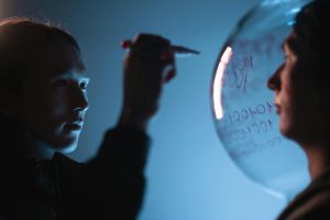 Person writing on a transparent sphere against a blue background with focused expression