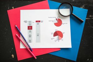 Overhead view of financial analysis charts with magnifying glass on colorful background, ideal for business concepts.