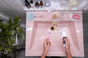 Overhead view of a pink ceramic sink with skincare items, green plant, and hygiene products.