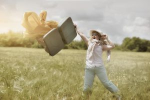 Happy woman in sunny field throwing suitcase joyously, embodying freedom and adventure.