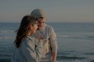 A couple enjoys a conversation by the sea on a windy day, captured in a serene moment.