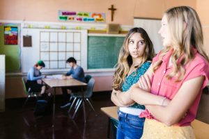 Teenage girls having a conversation in a school classroom setting.