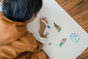A child creating drawings with markers on paper while sitting indoors.