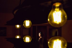 A bride poses elegantly in dramatic lighting surrounded by glowing bulbs, creating a unique wedding portrait.