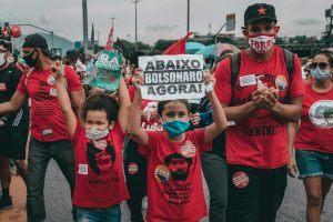 Protesters rallying against Bolsonaro in Rio de Janeiro, showing signs and wearing masks amidst the crowd.