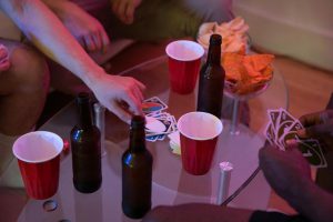 Friends enjoying a game night with cards, drinks, and snacks on a glass table.