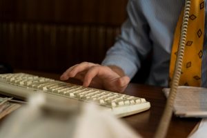 A close-up shot of a man typing on a vintage keyboard, dressed in business attire.