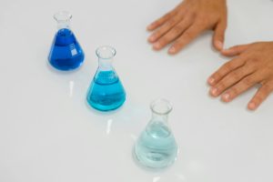Blue liquids in Erlenmeyer flasks on a lab table with hands visible, symbolizing science research.
