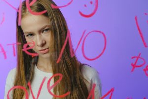 Teen girl with thoughtful expression behind written glass, moody studio shot.