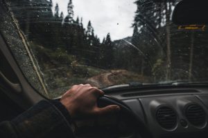 View from inside a car driving on a muddy forest road, capturing a hand on the steering wheel.