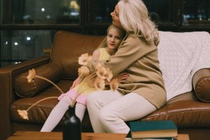 Grandmother and granddaughter hugging on a sofa, sharing a warm moment indoors.
