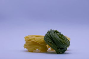 A close-up image showcasing raw yellow and green tagliatelle pasta bundles on a plain background.