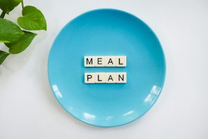 Innovative meal planning concept using alphabet tiles on a blue plate with green leaves.