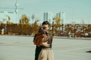 A warm embrace between a couple in a city parking lot with high-rise buildings.
