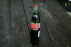 A classic Coca-Cola bottle placed on a rustic wooden table outdoors.
