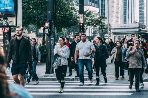 A diverse group of people crossing a street in a bustling city setting with skyscrapers.