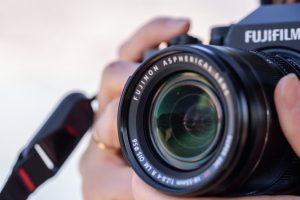 Detailed shot of a photographer holding a Fujifilm camera with a focus on the lens.