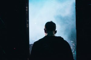 Back view of a DJ with headphones standing on stage in smoky atmosphere.
