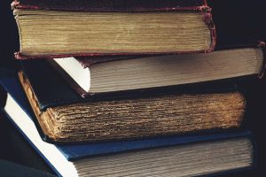 Close-up of a stack of vintage books with worn bindings, showcasing aged paper and textures.