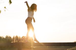 A young woman balancing on a fence during a serene sunrise, exuding freedom and joy.
