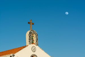 A stunning church facade with a cross and moon under a clear blue sky.
