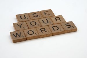 Wooden letter tiles spell 'USE YOUR WORDS' on a white background, promoting linguistic creativity.